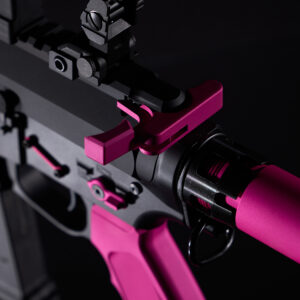 Custom pink charging handle on matte black tactical pistol close-up.