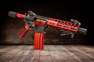 Custom red and black tactical rifle with suppressor on wooden backdrop.